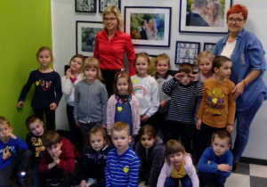 Zdjęcie całej grupy dzieci wraz z Panią fotograf i nauczycielką na tle ścianki ze zdjęciami.